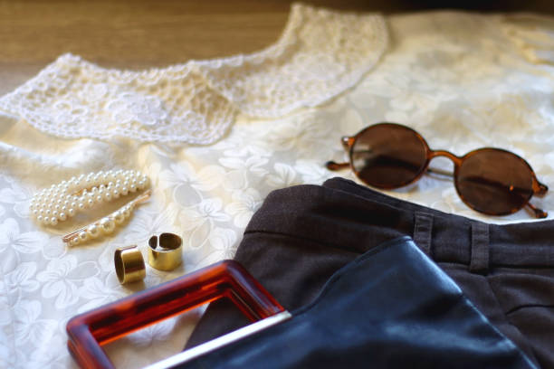 Vintage blouse, gray trousers, black bag, round sunglasses, pearl barrettes and brass rings. Outfit concept, selective focus.