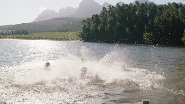 group of friends jumping in lake splashing in water having fun enjoying summer vacation