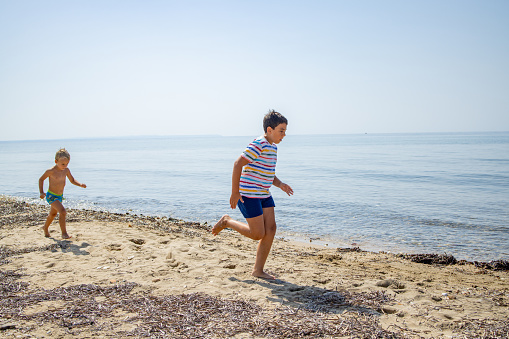 Playful Caucasian brothers running and playing on the beach during their holiday