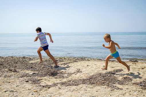 Side-view of Caucasian brothers running and playing on the beach during their holiday