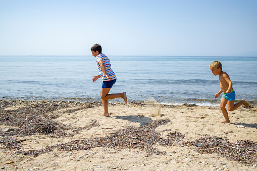 Side-view of Caucasian brothers running and playing on the beach during their holiday