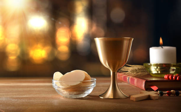 Cup of wine and hosts on wooden with backlights Cup of wine and hosts on wooden table with bible and candle for eucharist with backlights. Front view. religious text stock pictures, royalty-free photos & images