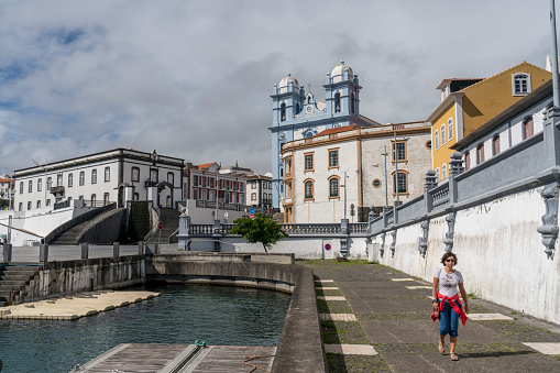 Women walking alone along the embankment in Angra do Heroismo, in background Church of Mercy, low angle view from the port, Terceira, Azores