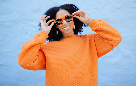 Fashion portrait, sunglasses and black woman isolated on blue background gen z, youth or trendy clothes. Happy person or beauty model in confidence, vision style and orange color on brick wall mockup