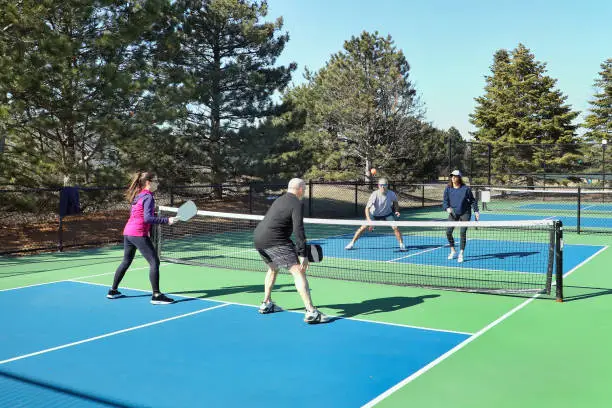 Photo of Men and Women in a Doubles Game of Pickleball