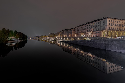 Scenic night view of a city canal illuminated by the streetlights in Murrazi, Turin, Italy