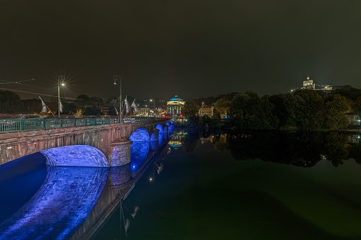 A stunning nighttime shot of a bridge illuminated in a beautiful blue light near the Gran Madre di Dio Church in Turin, Italy