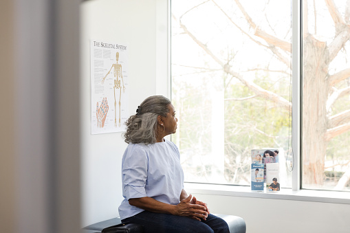 Mujer adulta mayor mira por la ventana en el consultorio del médico photo