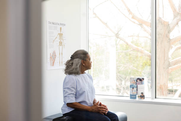 Senior adult woman stares out the window in doctor's office The senior adult woman sits in the doctor's office and stares out the window daydreaming. waiting stock pictures, royalty-free photos & images