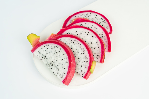 Several slices of red dragon fruit or pitaya lying on a white concrete tray