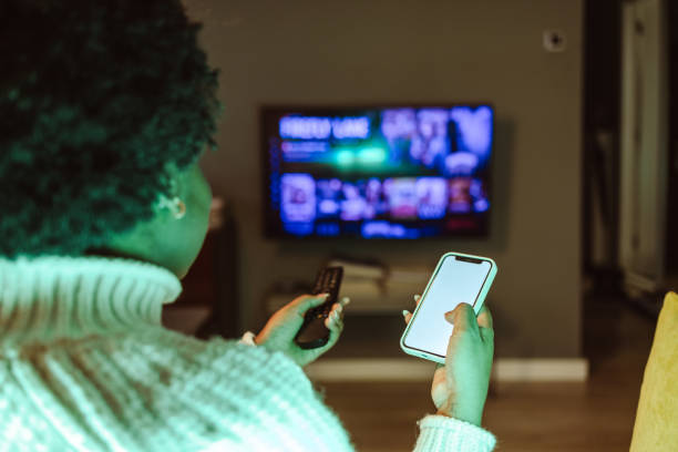 istock Young woman holding smart phone and TV remote control 1482029563