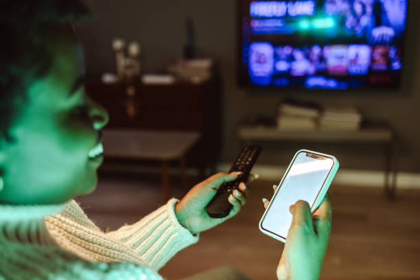 istock Young woman holding smart phone and TV remote control 1482029564