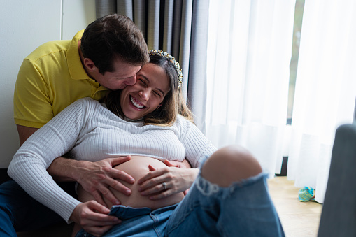 Latino married couple average age 30 to 40 years old formally dressed are lying on their bed enjoying the wife's pregnant belly, congratulations on this early arrival