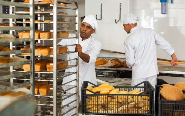 istock Man baker transporting a cart with bread in bakery 1482057077