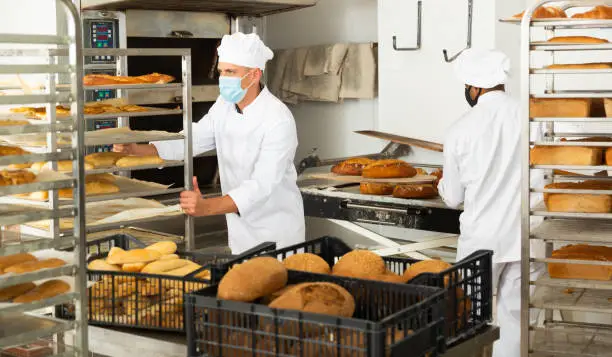 Photo of Male baker carrying rack trolley with bread