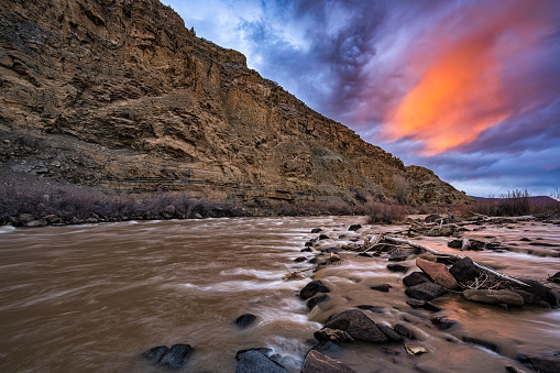 Colorado River Rapids and Clouds Time Lapse - Scenic view along the Colorado River with high canyon walls and fast moving clouds captured during sunset and into dusk. Motion showing moving water flowing downstream while clouds moving away and lighting up with vibrant color at sunset. High resolution 4K with slight camera motion movement.
