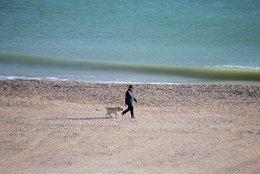 Mamaia, Romania – November 19, 2022: An adult male walking with a dog on the sandy beach of Mamaia resort