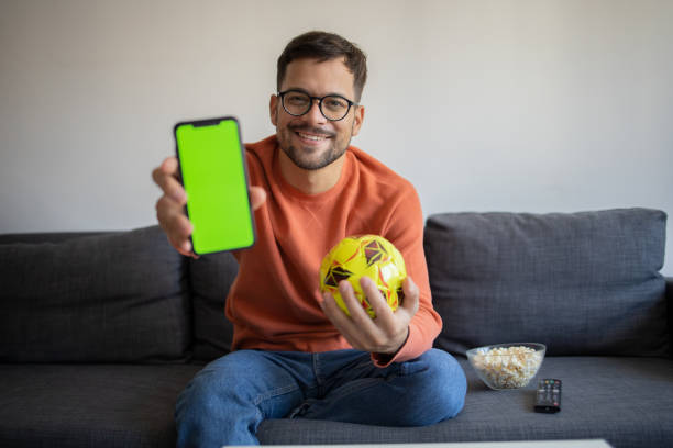 Excited man cheering while watching tv at home Handsome young man watching soccer match on TV at home soccer online free bets stock pictures, royalty-free photos & images