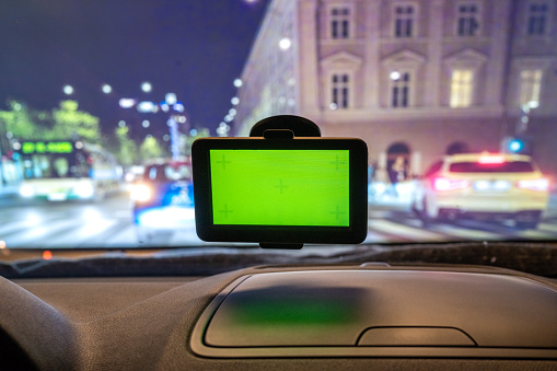 GPS navigator with green screen attached to car window while driving in city center at night.