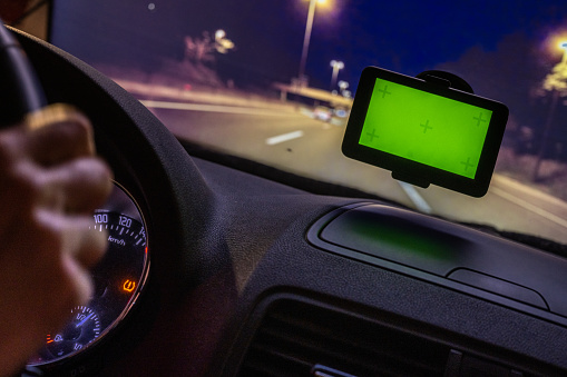Driver using GPS navigator with green screen while driving car on highway at night