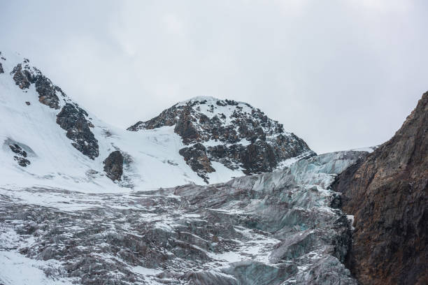 istock Dramatic landscape with large icefall on glacier under snow mountain peak in gray cloudy sky. Sharp rocks and beautiful glacier with icefall in high altitude. Gloomy scenery in mountains in overcast. 1482081165