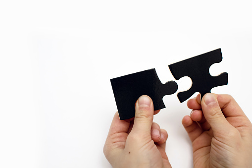 Two black puzzles in the hands of a child on a white background close-up. Puzzle for the development of children's intelligence. Connection concept with free space for text