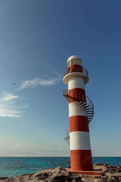istock Top of a white-red lighthouse against a blue sky with an airplane. 1482086265