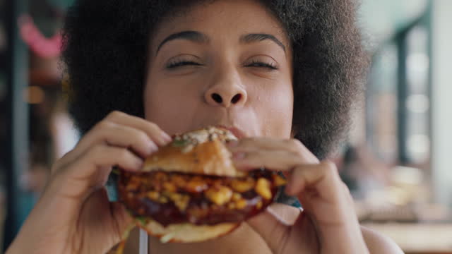 beautiful woman with afro eating burger in restaurant enjoying delicious juicy hamburger mouth watering meal african american female having lunch 4k
