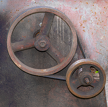 Large and small iron wheels on a pulley attached to dirty rusted metal panel