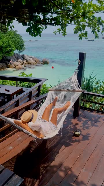 Koh Lipe Thailand Asian women in a hammock at the beach looking out over the turqouse colored ocean