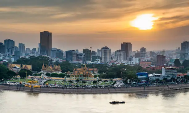 Rooftop view,looking across to the Riverside area of Cambodia's capital city.Sunset over Royal Palace and high rise buildings beyond, as a small boat drifts by towards the Mekong river.