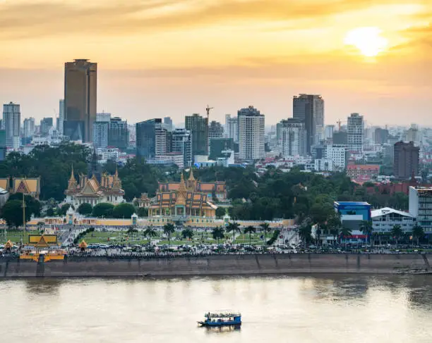 Rooftop view,looking across to the Riverside area of Cambodia's capital city.Sunset over Royal Palace and high rise buildings beyond, as a small boat drifts by towards the Mekong river.