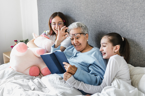 latin grandmother and granddaughter reading a book in bed at home in Latin America, hispanic women family