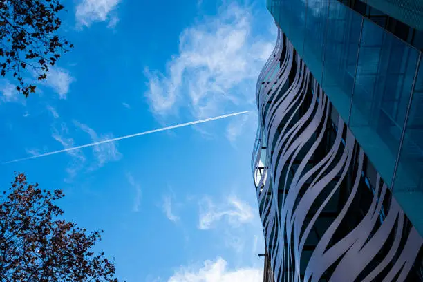 Photo of Sky trail crossing the blue sky in a urban scene with a building skyscraper facade in Barcelona, Catalonia