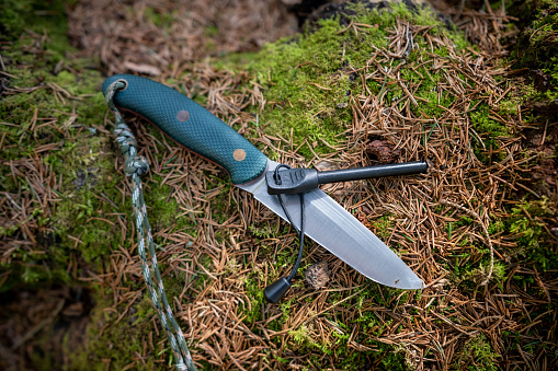 Bushcraft knife and flint steel on a mossy stump covered by pine tree needles