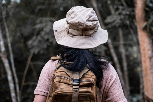 Back view of a young woman with backpack hiking in the deep jungle