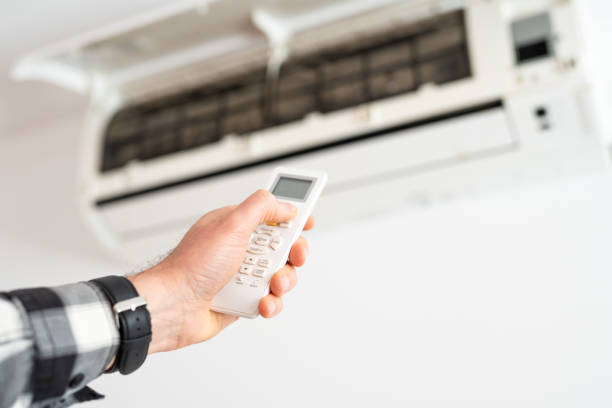 A man's hand holds a remote control from an air conditioner with a temperature on the screen of 21.