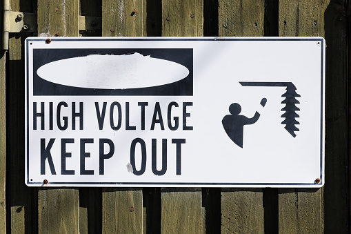 High voltage keep out sign on a wooden gate. The red parts have faded away.