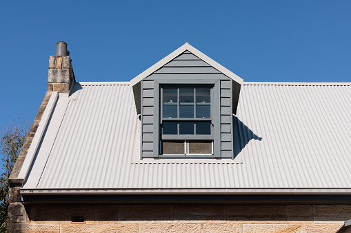 Top of a building with one window and blue sky above.