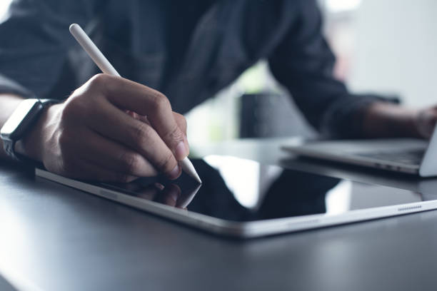 istock Business man, graphic designer using stylus pen on digital tablet screen while working on laptop computer on office table. Man in casual ware online working, surfing the internet on tablet pc 1482129344