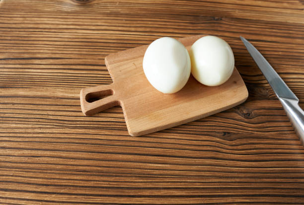 due uova sode su un'asse di legno con un coltello. - two eggs foto e immagini stock