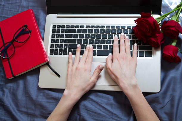 Hands, computer keyboard, bed top view. Workplace background, work at home, notepad and flowers