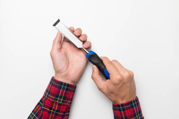 Hand tool chisel on a white background in a man's hand, top view. Craftsman in a plaid shirt holds a carpentry hand cutting tool stock photo