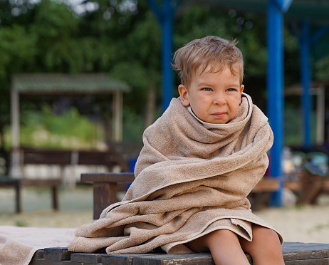 The little boy wrapped in towel for warming, sad facial expression. A little boy on the seashore