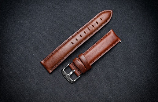 Luxury, minimalist brown tanned leather watch strap on a black surface background.