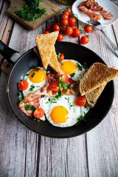 istock Fried eggs with bacon and fresh tomatoes. On a wooden background 1482140423