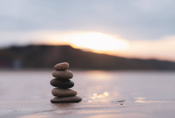 pietra della pila zen sulla spiaggia di sabbia del mare con sfondo sfocato del tramonto, concetto di piramide della torre di roccia di ghiaia del paesaggio dell'immagine per la stabilità, l'armonia, l'equilibrio della vita, la meditazione, lo zen come - cornerstone stability pyramid stone foto e immagini stock