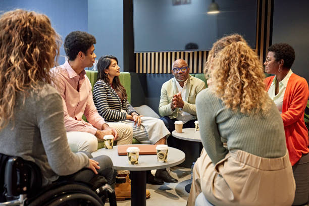 Informal business meeting in modern office Multiracial male project manager in late 50s talking with diverse team enjoying coffee and update on planning and development. ethnic diversity stock pictures, royalty-free photos & images