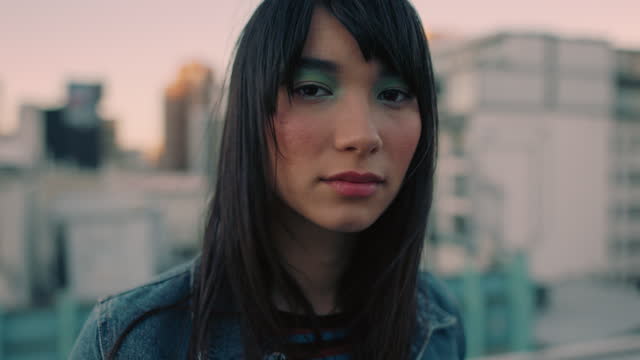 portrait beautiful young asian woman on rooftop at sunset wearing colorful makeup looking confident in urban city