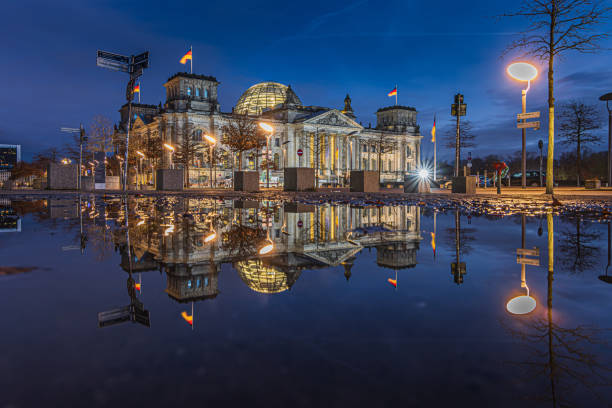 Reichstag in Berlin at the blue hour. Illuminated buildings and street lamps in the evening. Reflection of building on water surface. Evening mood in the winter of the capital of Germany